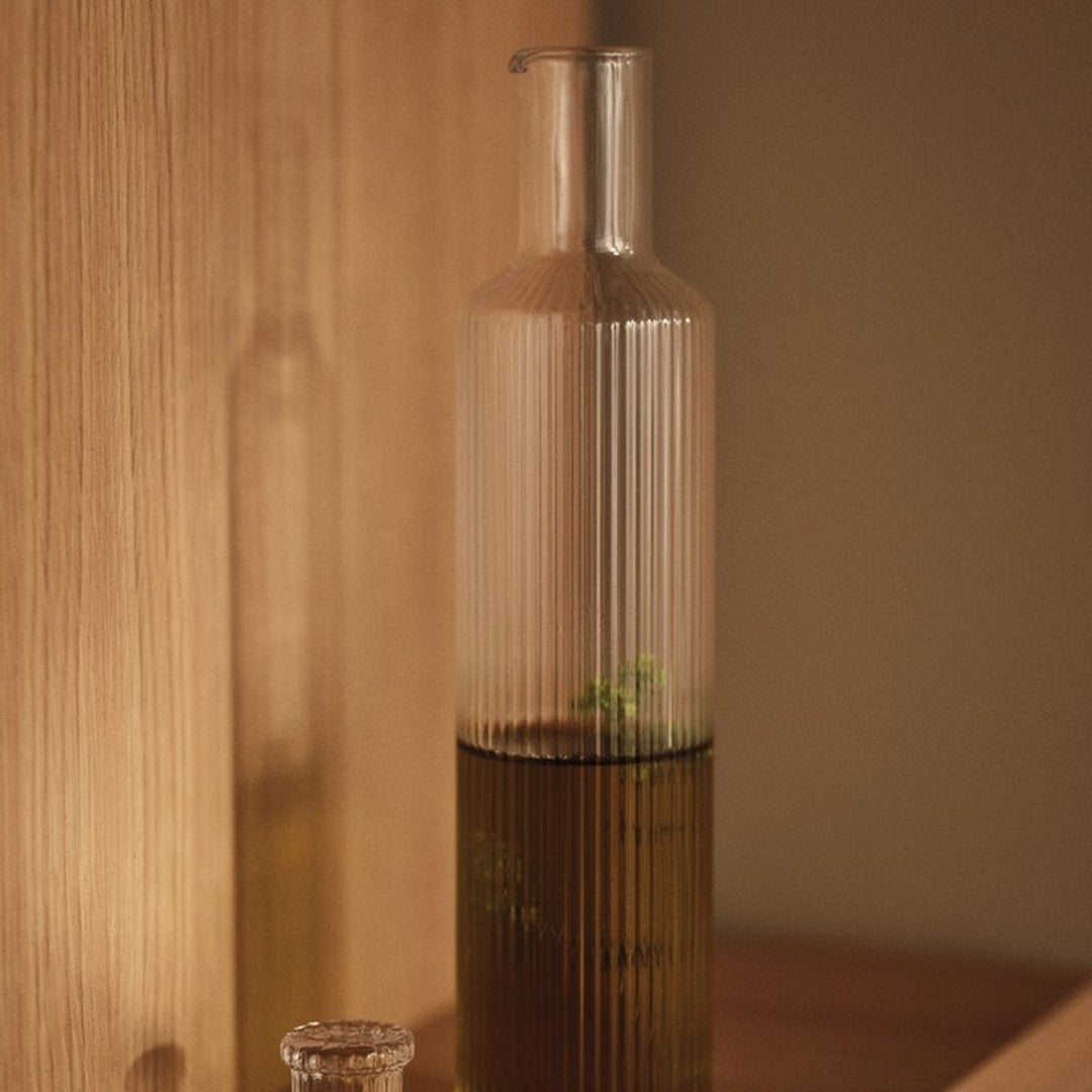 Clear glass bottle with ribbed texture, featuring a gradient from transparent to dark green liquid.