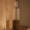 Clear glass bottle with ribbed texture, featuring a gradient from transparent to dark green liquid.