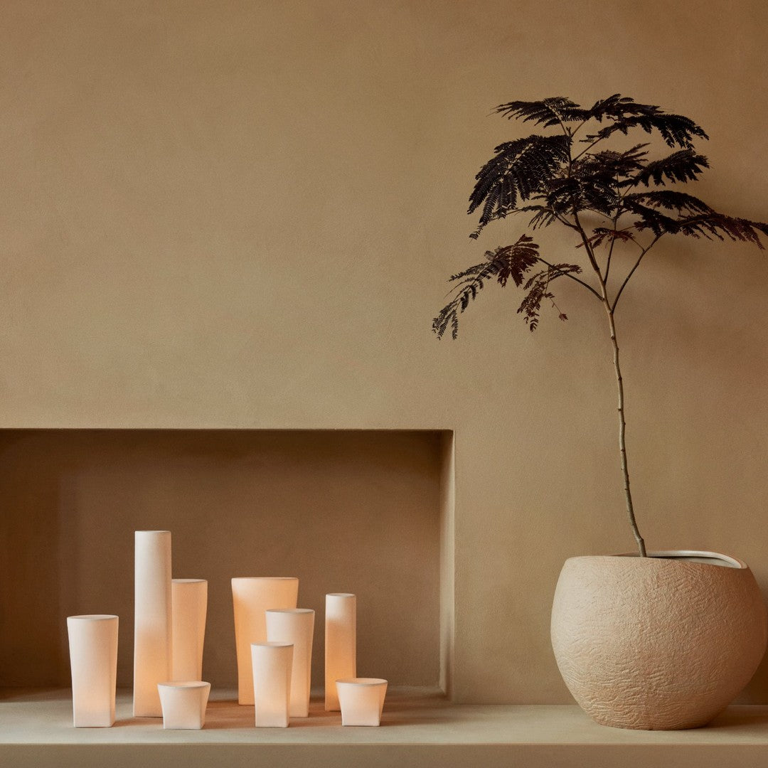 Set of warm beige and soft white candle holders against an earthy tan backdrop, featuring subtle textures and shapes.