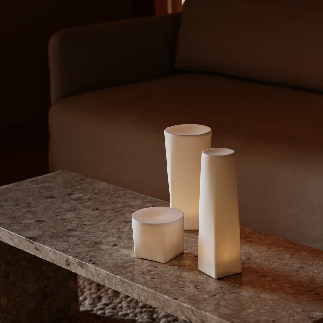 White geometric candles on a textured stone table, contrasting against a warm brown sofa background.