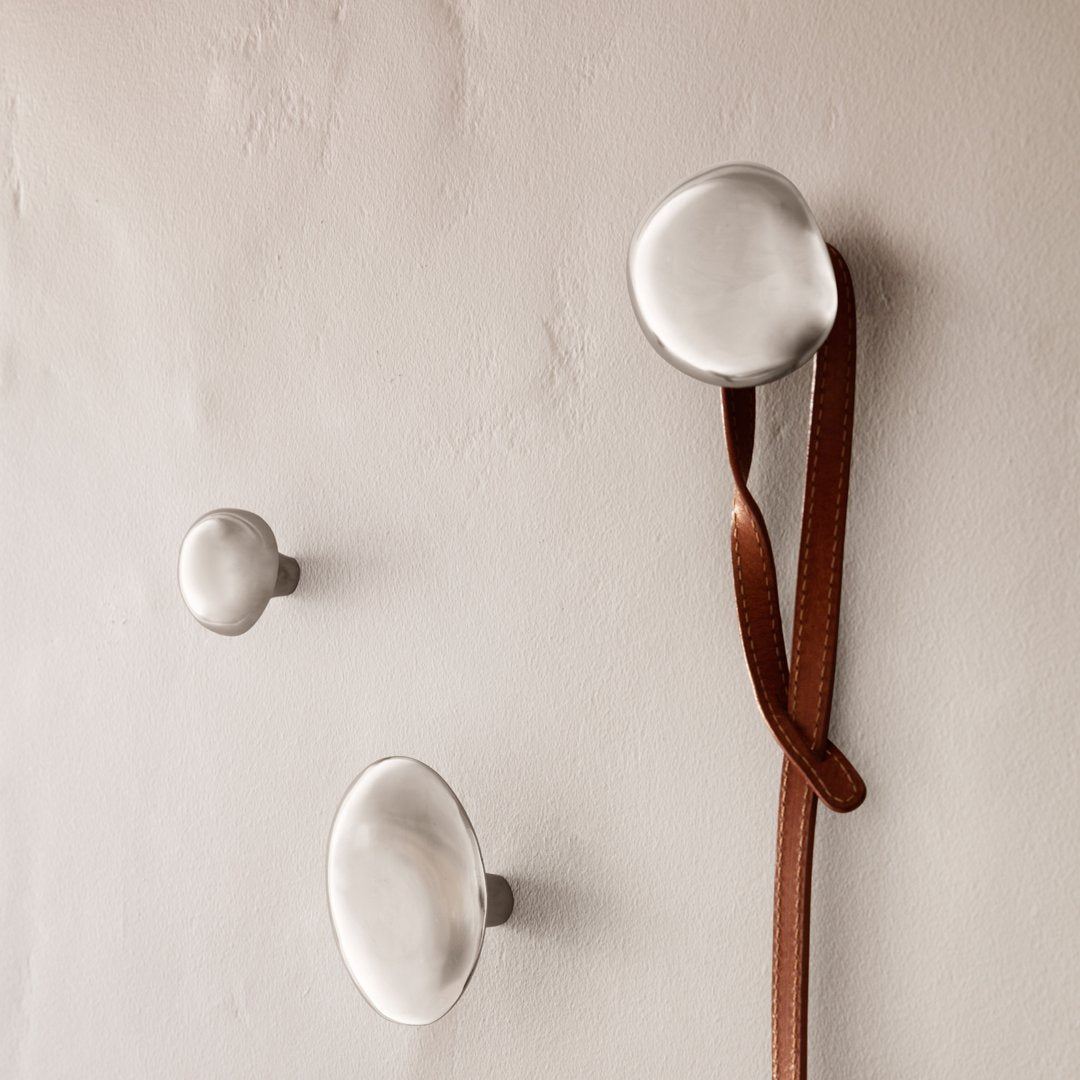 Sleek metallic wall hooks in silver tones with a smooth, rounded design against a neutral background.