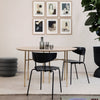 Minimalist round table with natural wood finish, black chairs, and a neutral rug, accented by framed art on the wall.