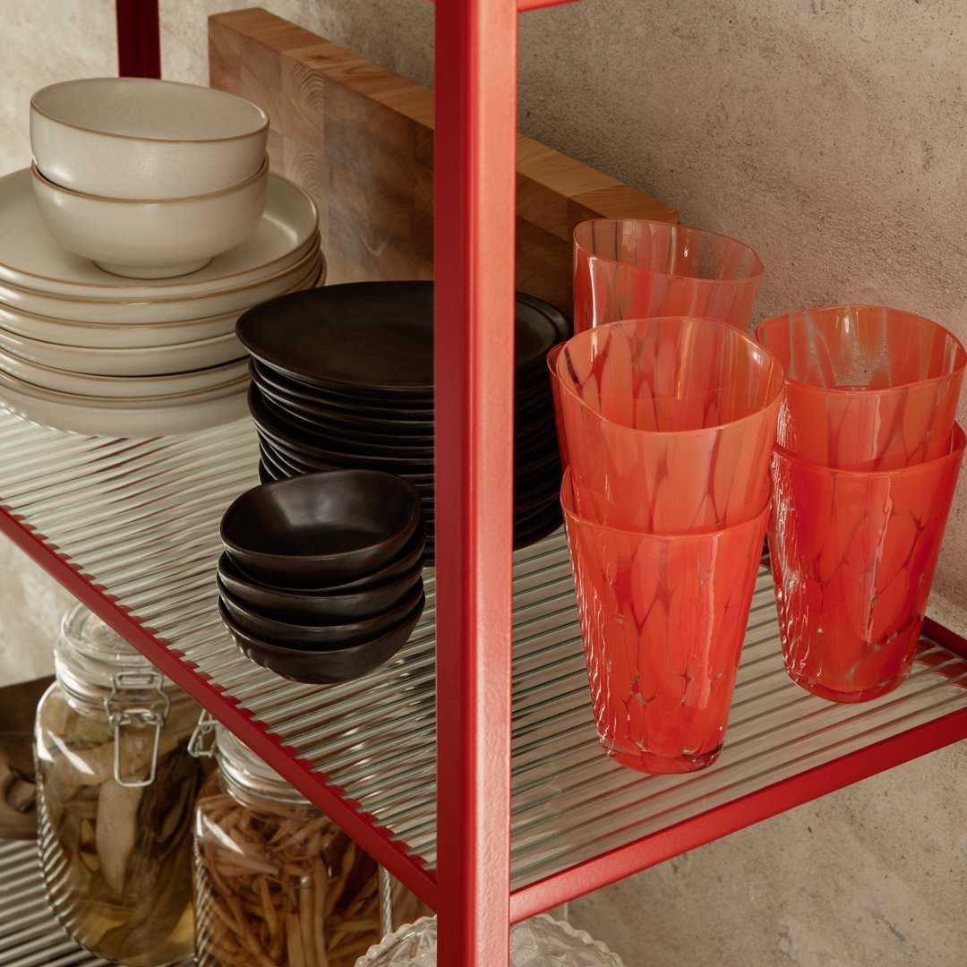 Colorful glassware in vibrant red patterns, with contrasting black and neutral dishware on a metal shelf.