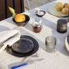 "Elegant black dishware and glass on a neutral tablecloth, accented by fresh oranges and earthy-toned fruits."