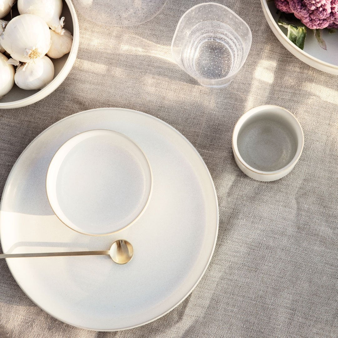 Elegant neutral dinnerware set featuring soft white tones and minimalistic design on a textured linen tablecloth.