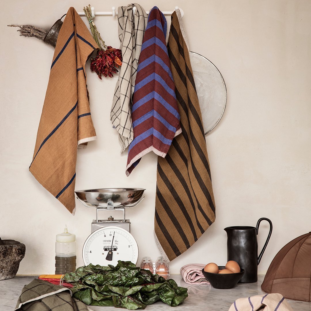 "Set of vibrant kitchen towels in warm brown, bold blue, and classic checked patterns, hanging stylishly in a rustic setting."