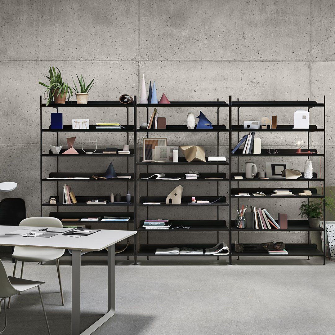 "Modern black shelving unit with a mix of geometric decor, books, and plants against a concrete backdrop."