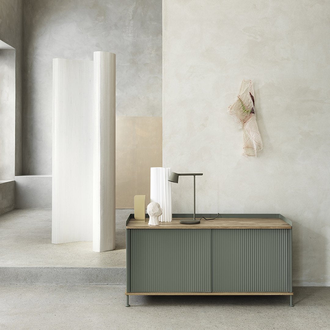 Sleek green and light wood sideboard against a neutral cement backdrop with soft white and beige accents.