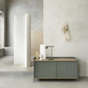 Sleek green and light wood sideboard against a neutral cement backdrop with soft white and beige accents.