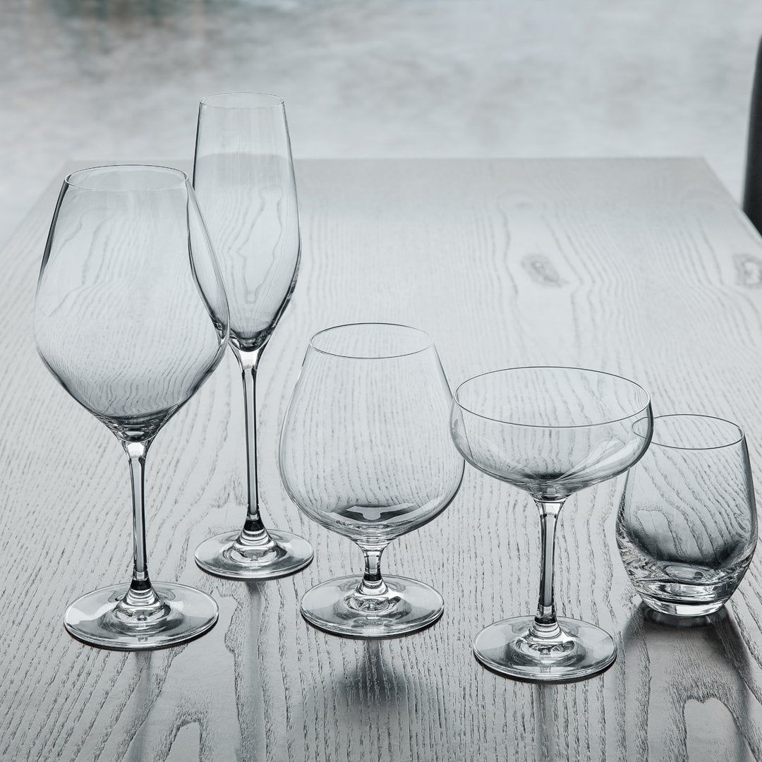 Set of five elegant, clear glass drinkware pieces showcasing sleek shapes and smooth finishes on a wooden surface.