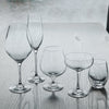 Set of five elegant, clear glass drinkware pieces showcasing sleek shapes and smooth finishes on a wooden surface.