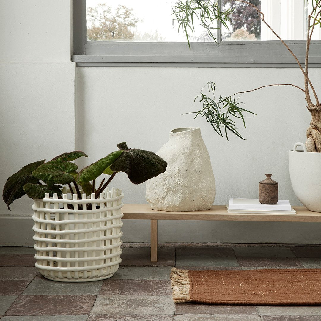 White woven plant basket with a textured design, surrounded by earthy tones and natural textures in a minimalistic setting.