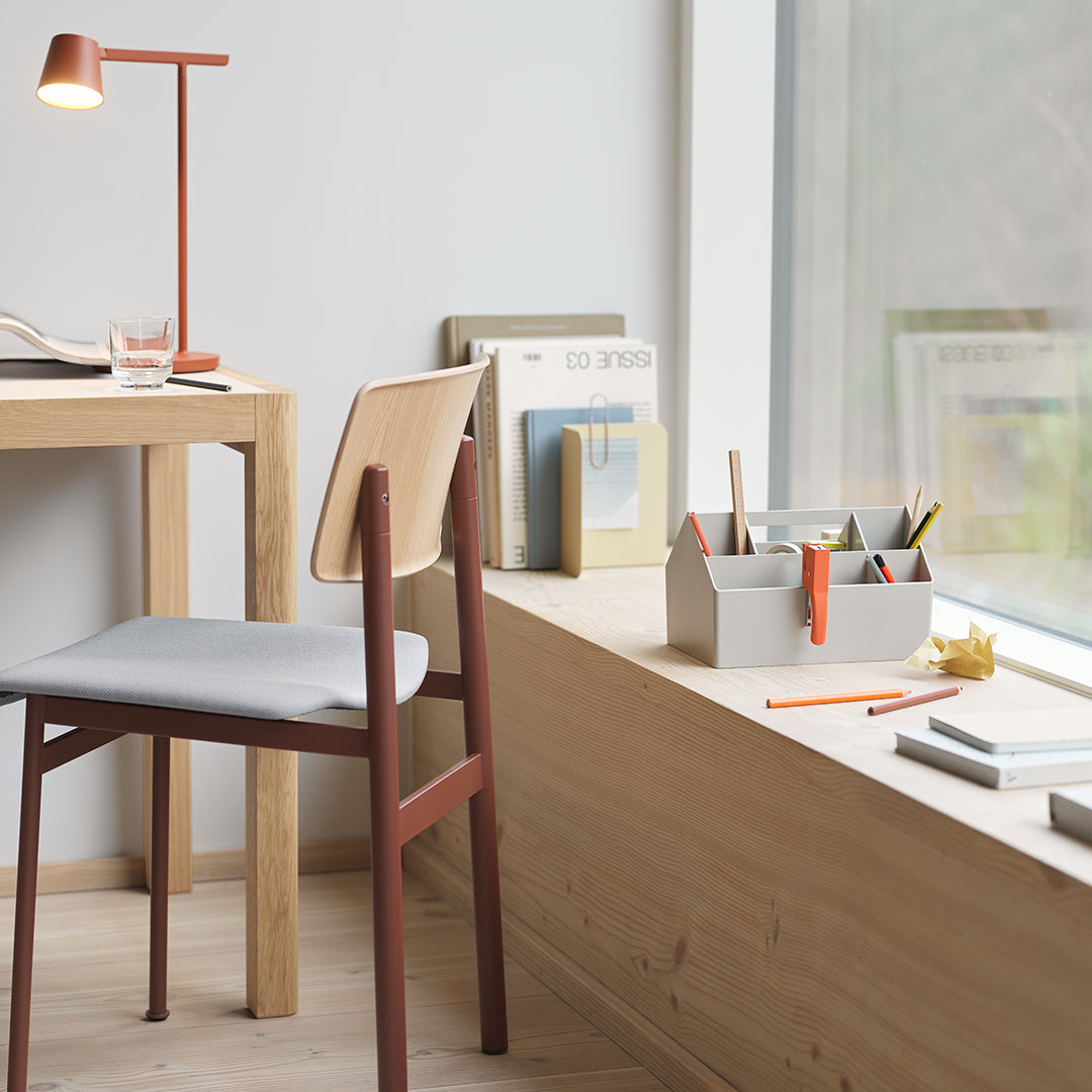 Modern desk scene featuring a light wood finish, a gray seat with reddish-brown accents, and pastel stationery items.