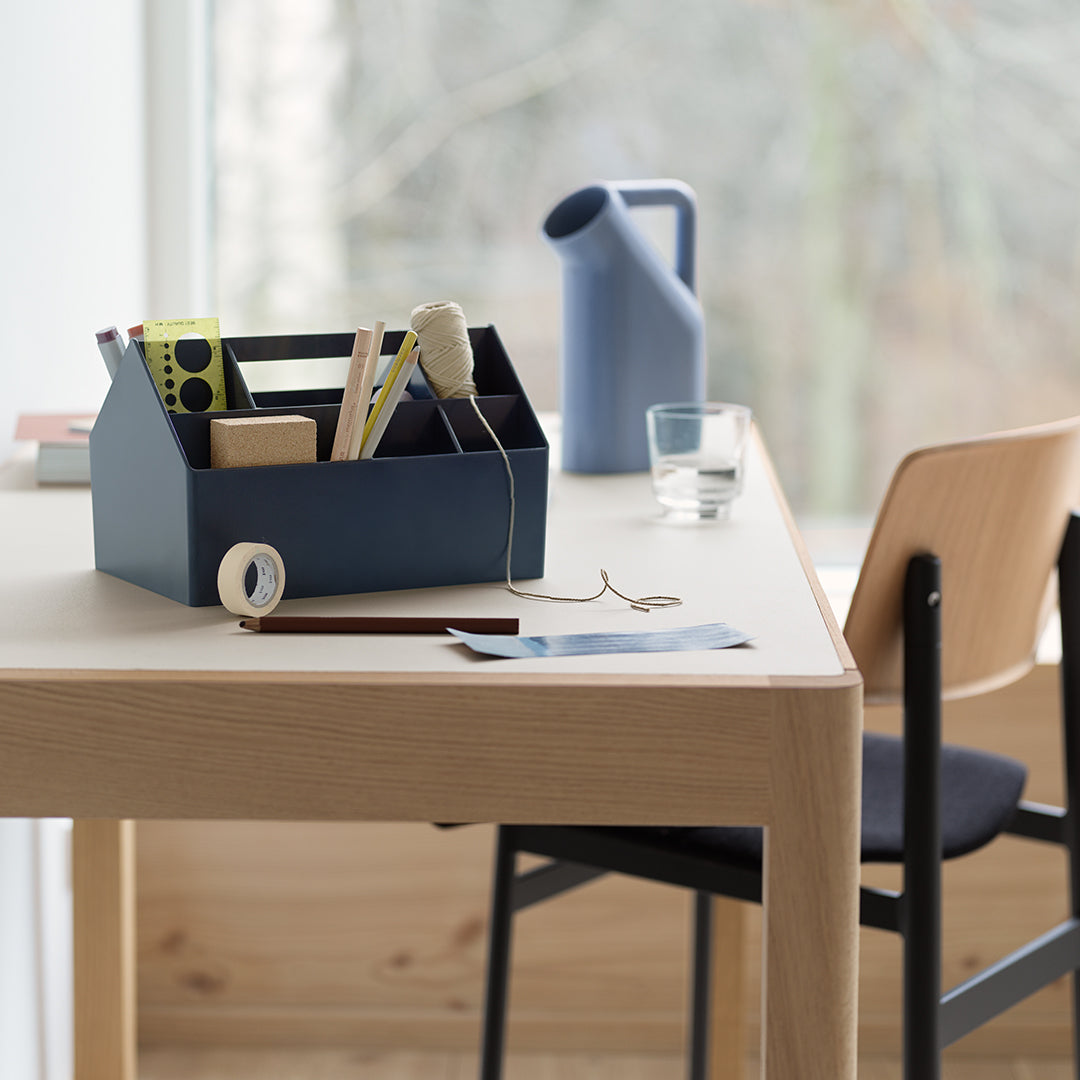 Navy blue storage caddy with assorted office supplies, wooden table, minimalist design, and neutral color palette.