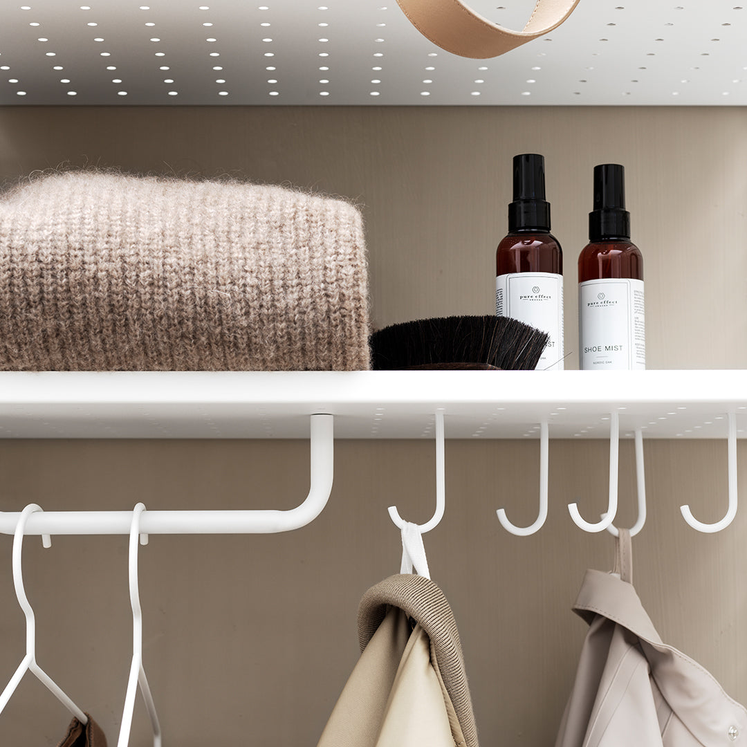 Cozy beige sweater on a white shelf with black and brown spray bottles against a neutral backdrop.